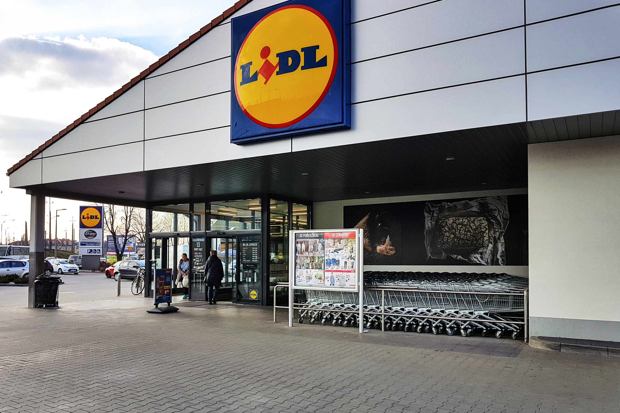 Magazin Lidl cu sigla oficială la intrare, panou de oferte promoționale și cărucioare