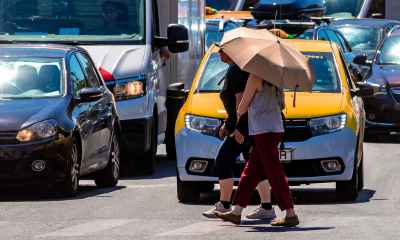 Pietoni protejați de umbrelă împotriva soarelui și a caniculei pe trecerea de pietoni