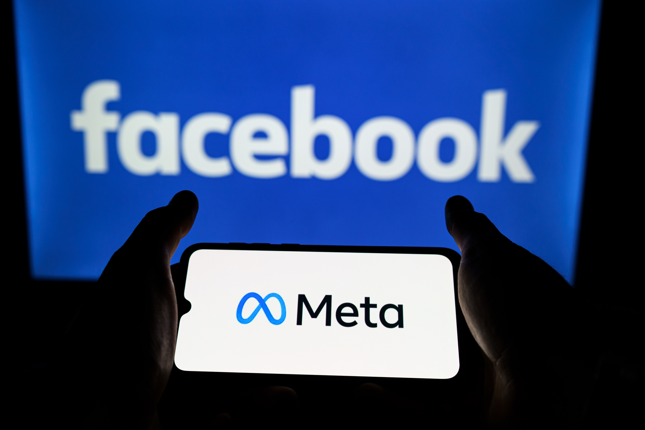 Smartphone cu sigla companiei Meta pe fundalul ecranului cu logo-ul Facebook