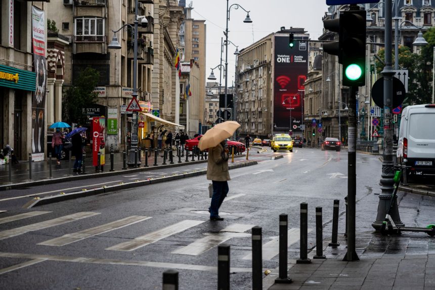Oameni cu umbrele pe o stradă din București într-o zi ploioasă de toamnă