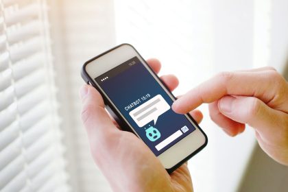 Mâini care țin un telefon cu o aplicație de chat cu inteligență artificială deschisă pe ecran