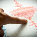 Seismograf care înregistrează unde seismice pe hârtie milimetrică, cu un deget care arată graficul