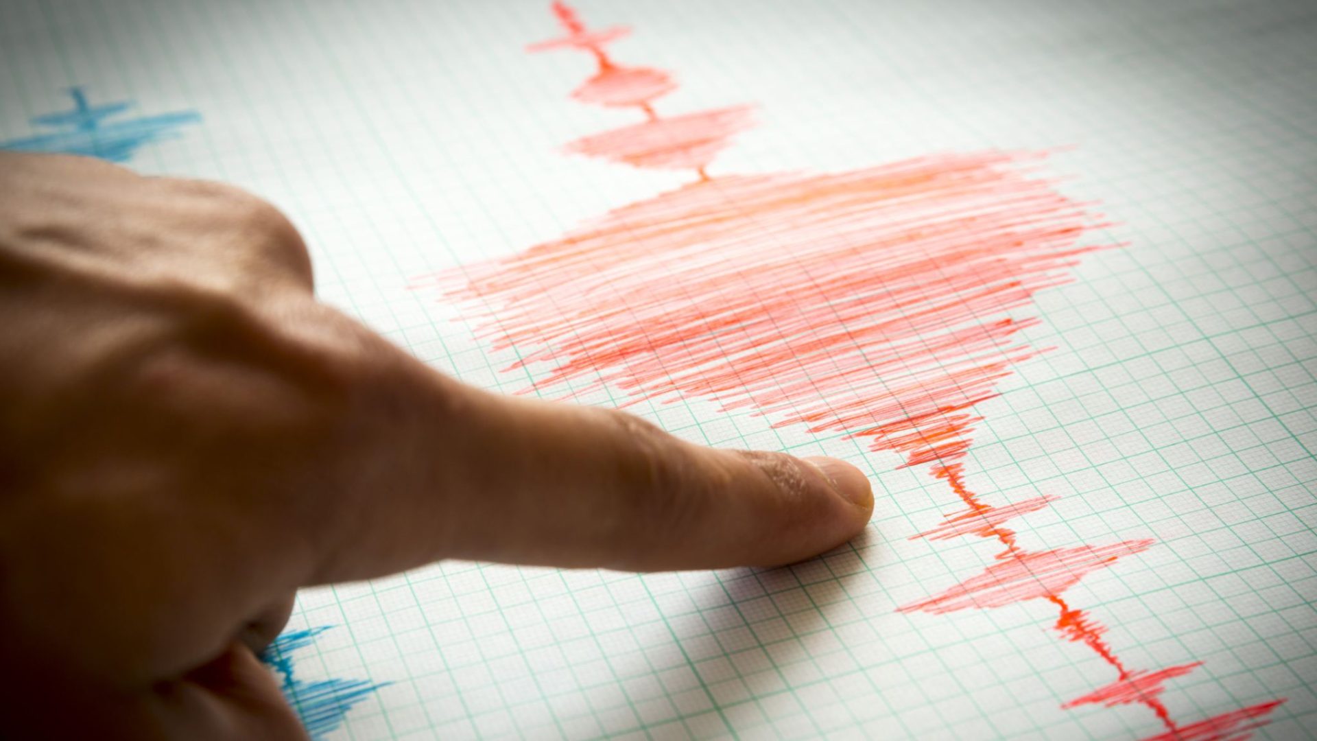 Seismograf care înregistrează unde seismice pe hârtie milimetrică, cu un deget care arată graficul