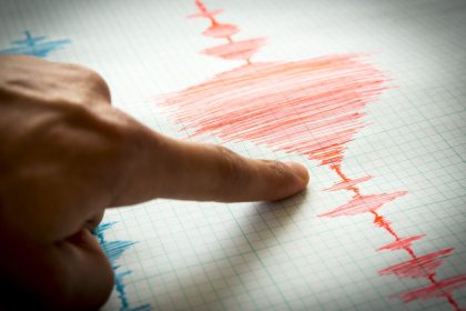 Seismograf care înregistrează unde seismice pe hârtie milimetrică, cu un deget care arată graficul