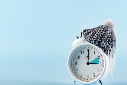 Ceas deșteptător pe noptieră, lângă un pat, într-o seară de toamnă